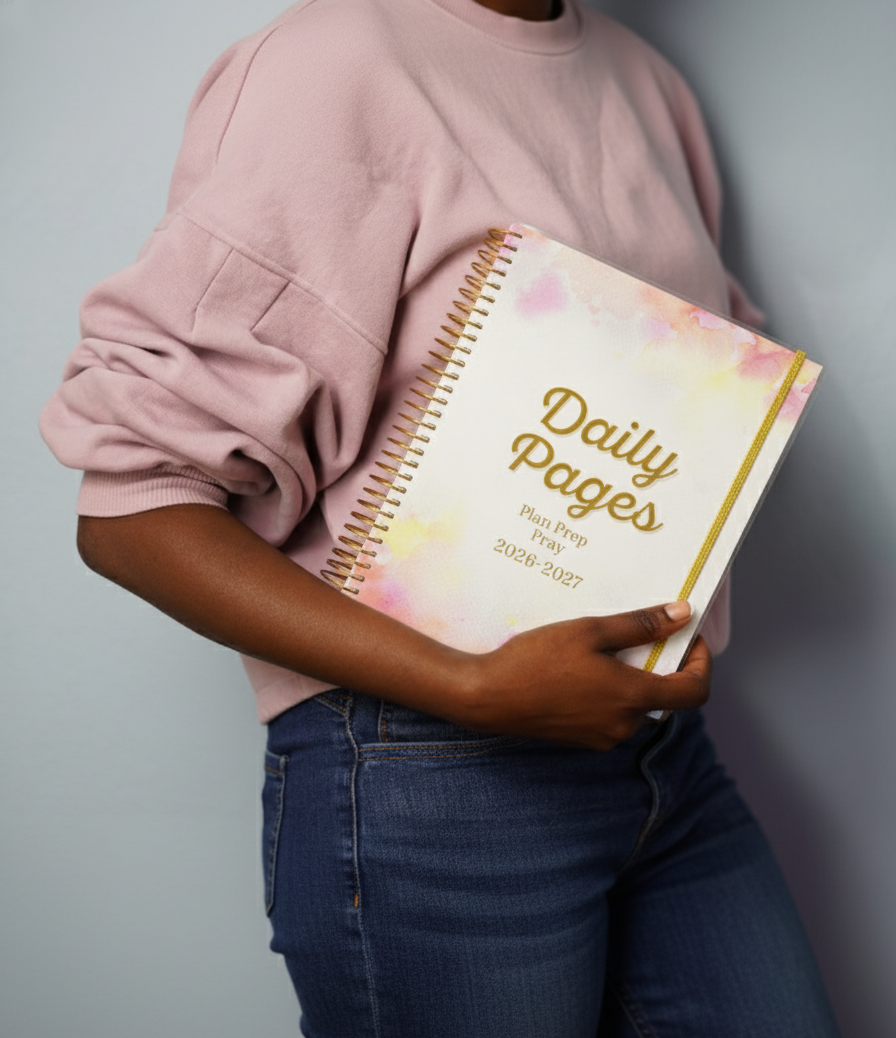 Person holding a planner titled 'Daily Pages' with a floral design on a plain background